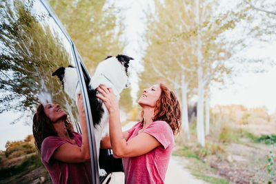 Side view of woman holding dog through car window