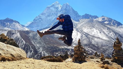 Full length of man jumping against snowcapped mountains