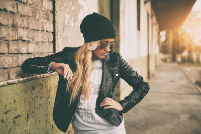 Fashionable young woman wearing jacket smoking cigarette outdoors
