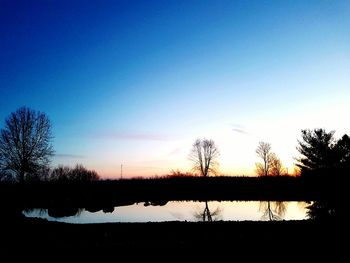 Silhouette of bare trees in lake during sunset