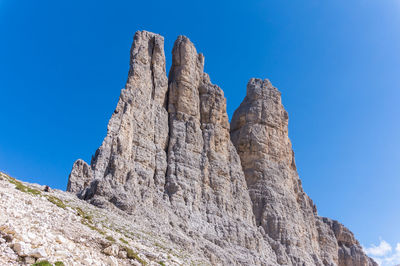 Low angle view of rocky mountain against clear blue sky