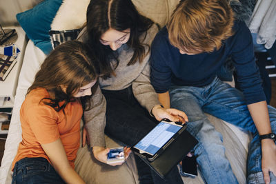 High angle view of friends using technology while sitting on bed at home