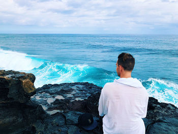 Rear view of man looking at sea sitting against sky