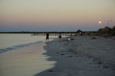 People at beach against sky during sunset