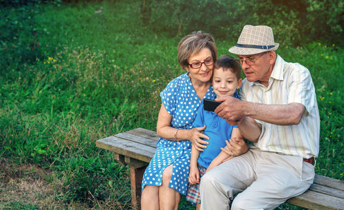 Family taking selfie through mobile phone while sitting on bench in park