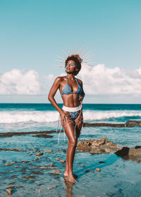 Full length of young woman standing on beach against sky