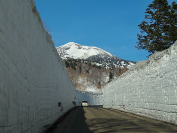 Road amidst snowcapped mountains against clear sky