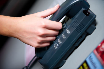 Close-up of human hand holding telephone on wall