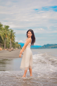 Portrait of woman standing on beach against sky.