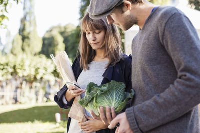 Young couple using mobile phone while buying vegetables in market