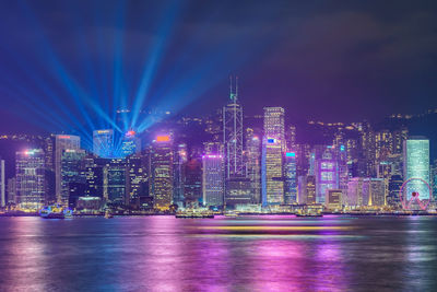 Illuminated buildings by river against sky in city at night