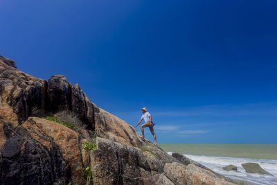 Man standing on rock by sea against blue sky