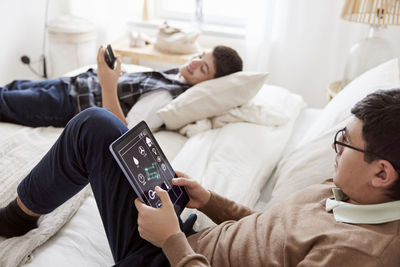 Brothers lying on bed and using phone and tablet