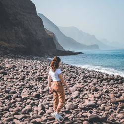 Rear view of woman on rock at beach against sky