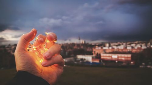 Close-up of hand holding illuminated cityscape against sky