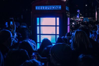 People photographing illuminated telephone booth at night
