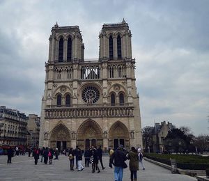 Tourists in front of building against cloudy sky