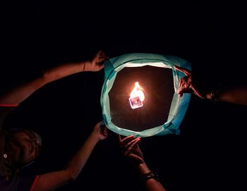 Close-up of hand holding lit paper / sky lantern against black background on diwali