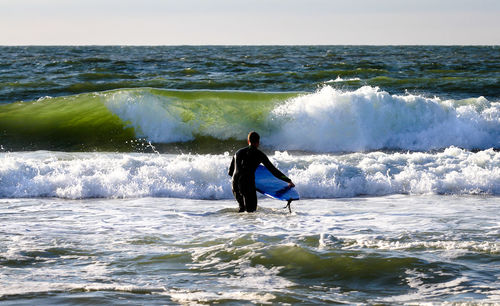 Rear view of surfer with surfboard standing in sea