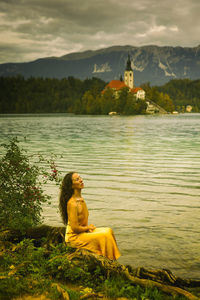 Woman in yellow dress sitting on the shores of lake bled, slovenia ii