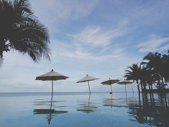 Parasols by infinity pool at resort against cloudy sky