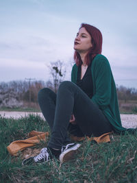 Young woman looking away while sitting on land