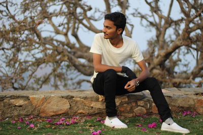 Young man looking away while sitting on tree