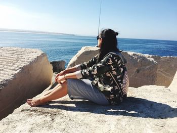 Woman sitting on retaining wall by sea against sky