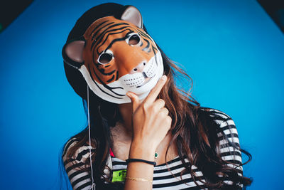 Portrait of woman wearing tiger mask against blue wall