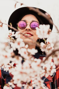 Close-up of woman wearing sunglasses and hat amidst pink flowers