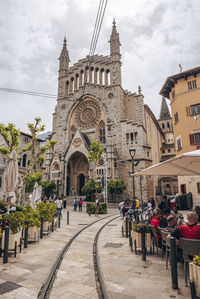 Railroad tracks by church of sant bartomeu de soller by restaurant against sky