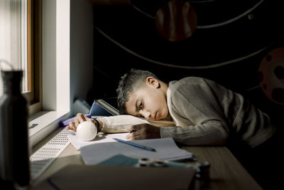 Tired pre-adolescent boy resting head on table in bedroom