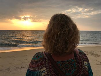 Rear view of woman on beach against sky during sunset