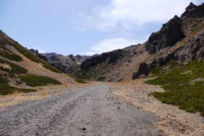 Dirt road by mountains against sky