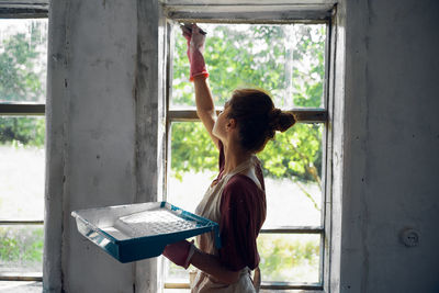 Young woman painting window at home