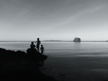 Silhouette boys on rocks at beach against sky