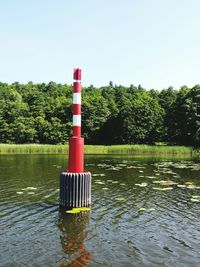 Red lighthouse by lake against clear sky