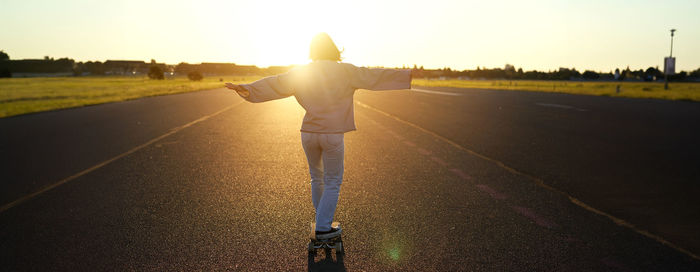 Rear view of man standing on road against sky during sunset