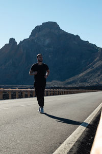 Rear view of man standing on road against mountains