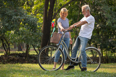 Man riding bicycle by woman against trees in park