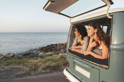 Female and male friends looking at sea from camping van during road trip