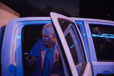 Young woman sitting in open truck and looking at cell phone