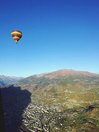 Hot air balloon flying over mountains against clear blue sky