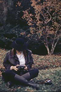 Full length of woman holding camera sitting in forest