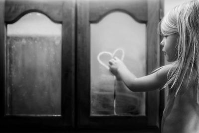 Rear view of girl making heart shape on mirror