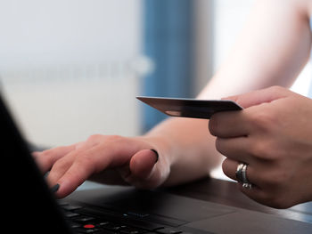 Close-up of woman holding credit card while using laptop