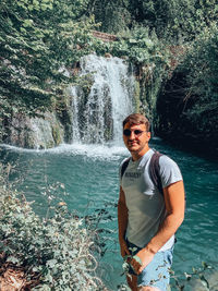 Portrait of young man standing against waterfall