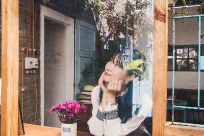 Young woman holding flower while standing by window