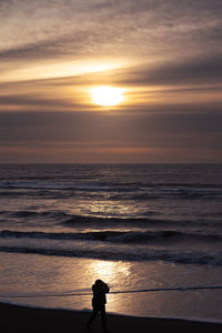 Silhouette woman standing at beach against sky during sunset