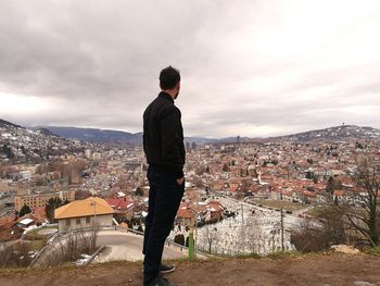 Rear view of man looking at cityscape against sky